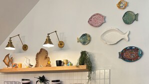 Una cocina con un refrigerador de acero inoxidable, estantes de madera con diversos platos, y una decoración de pescado montada en la pared.