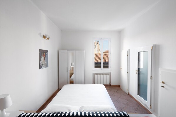 A bedroom with a bed, a radiator, a window, and a door.