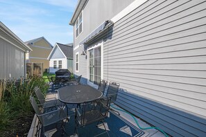 Eine Terrasse mit rundem Tisch, Stühlen, einem Grill und einem Gartenschlauch.