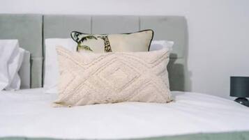 A bed with a patterned pillow and a plain pillow on a white mattress.