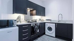 A modern kitchen with dark cabinets, a microwave, a stove, a washing machine, and a sink. - Old Dutch Embassy by Guestz (Kingston-upon-Hull)