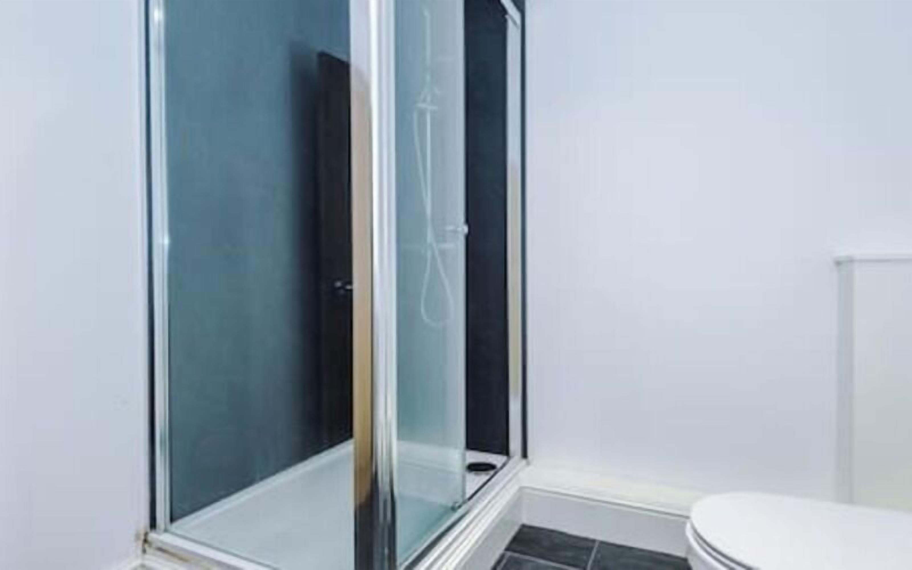 A bathroom with a glass-enclosed shower, a white toilet, and a tiled floor.