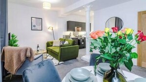 A modern living room with a green sofa, a dining table set with plates, and a vase of flowers. - Old Dutch Embassy by Guestz (Kingston-upon-Hull)