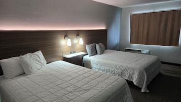 A hotel room with two beds, a nightstand, a wall-mounted light fixture, and a window with curtains.