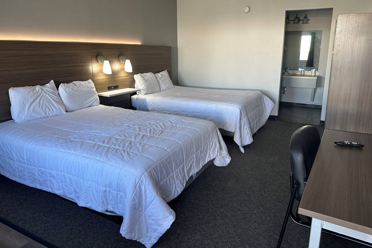 A hotel room with two beds, a desk, a chair, and a bathroom visible through an open door.