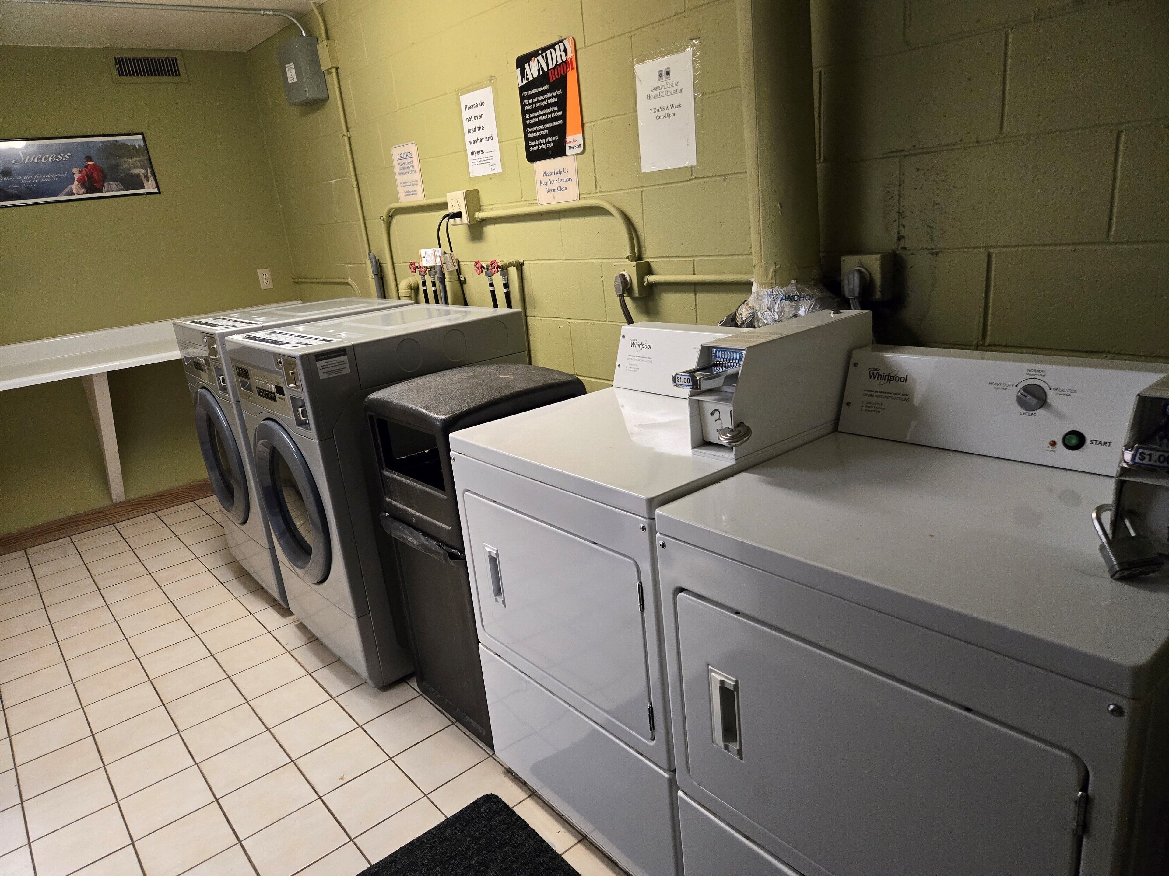Une buanderie équipée d’un lave-linge et d’un sèche-linge Whirlpool, d’un lave-vaisselle Whirlpool et d’un réfrigérateur Whirlpool. Des panneaux affichés au mur indiquent les règles à respecter dans la buanderie, et un panneau indique « Buanderie ».