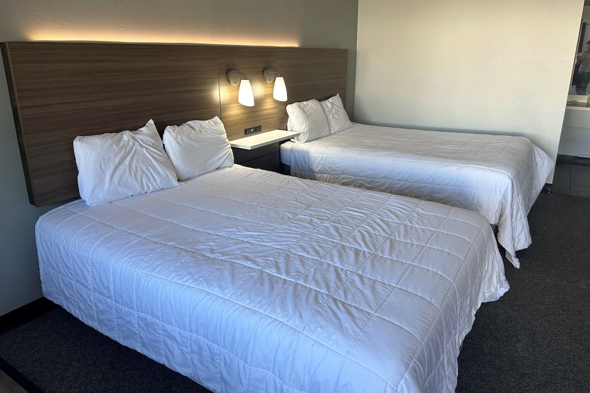 A hotel room with two single beds, a wooden headboard, bedside lamps, and a clock on the wall.