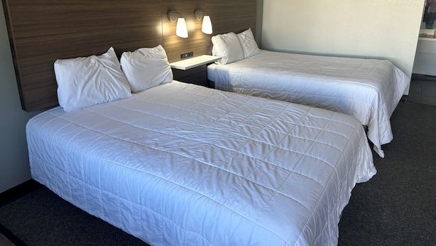 Ett hotellrum med två separata sängar, en sänggavel i trä, sänglampor och en väckarklocka på väggen.