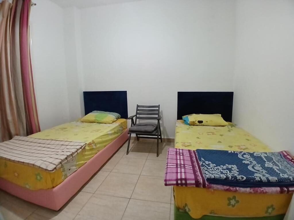 Une chambre avec deux lits simples, une chaise et un rideau.