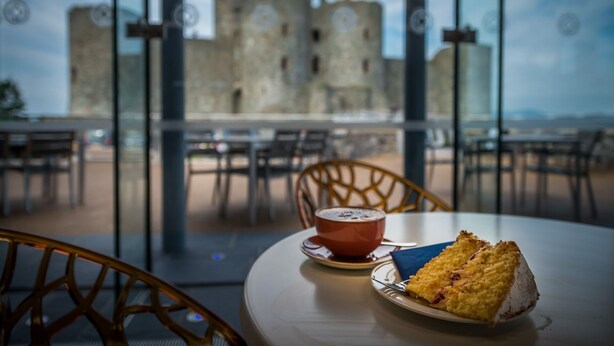 A table with a slice of cake and a cup of coffee, overlooking a historic castle.
