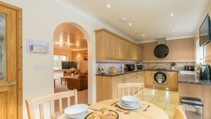 A modern kitchen with wooden cabinets, a dining area with a table set for two, and a TV in the living room.
