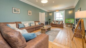 A spacious living room with a brown leather sofa, a wooden coffee table, and a television. - Beautiful Farmhouse Accommodation in a Country Setting | Hendre-Feinws (PWLLHELI)