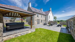 A stone building with a covered patio area, outdoor seating, and a hot tub. - Beautiful Farmhouse Accommodation in a Country Setting | Hendre-Feinws (PWLLHELI)