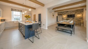 A spacious kitchen with a central island, a dining area with a stone accent wall, and a large window providing natural light. - Beautiful Farmhouse Accommodation in a Country Setting | Hendre-Feinws (PWLLHELI)