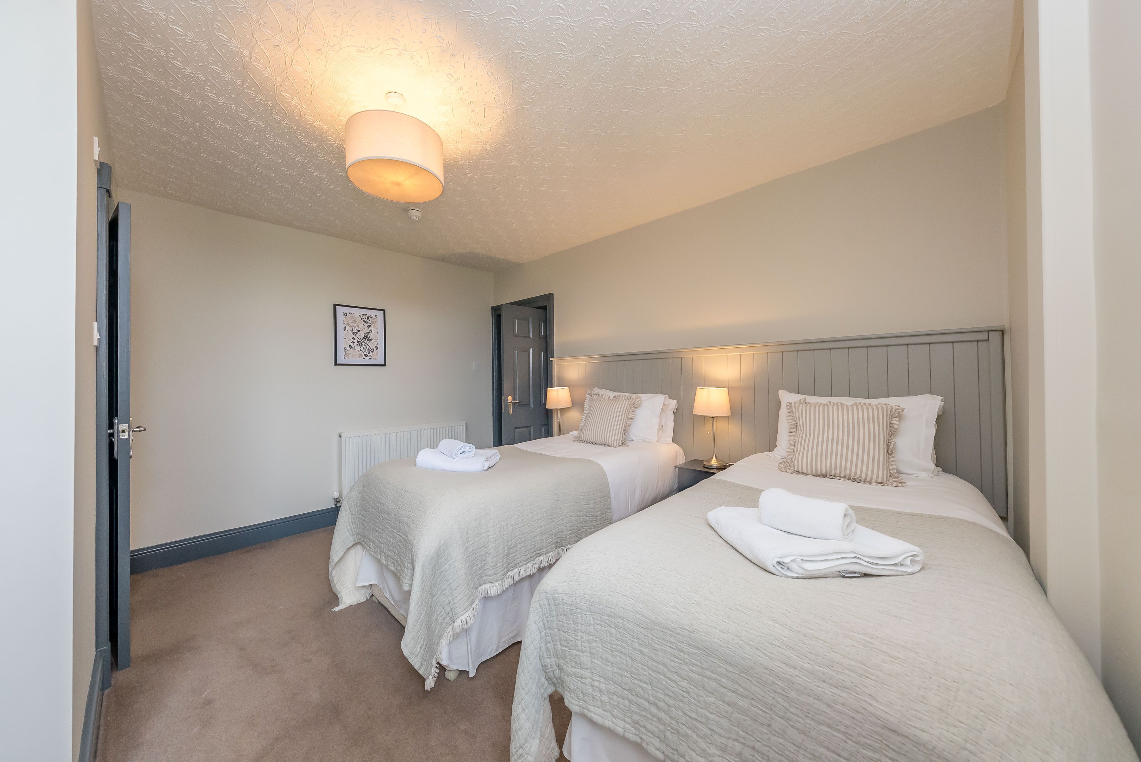 A hotel room with two beds, a radiator, a door, and a ceiling light fixture.