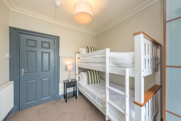 A bedroom with a bunk bed, a bedside table with a lamp, a door, and a radiator.