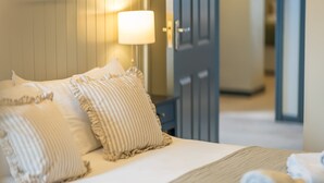 A neatly made bed with striped pillows and a rolled towel, a bedside lamp, and a door in the background. - Large Detached Property Walking Distance To The Beach | Llywelyn-Fawr (Aberffraw)