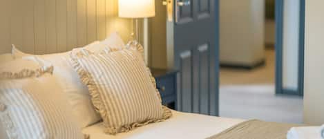 A neatly made bed with striped pillows and a rolled towel, a bedside lamp, and a door in the background.