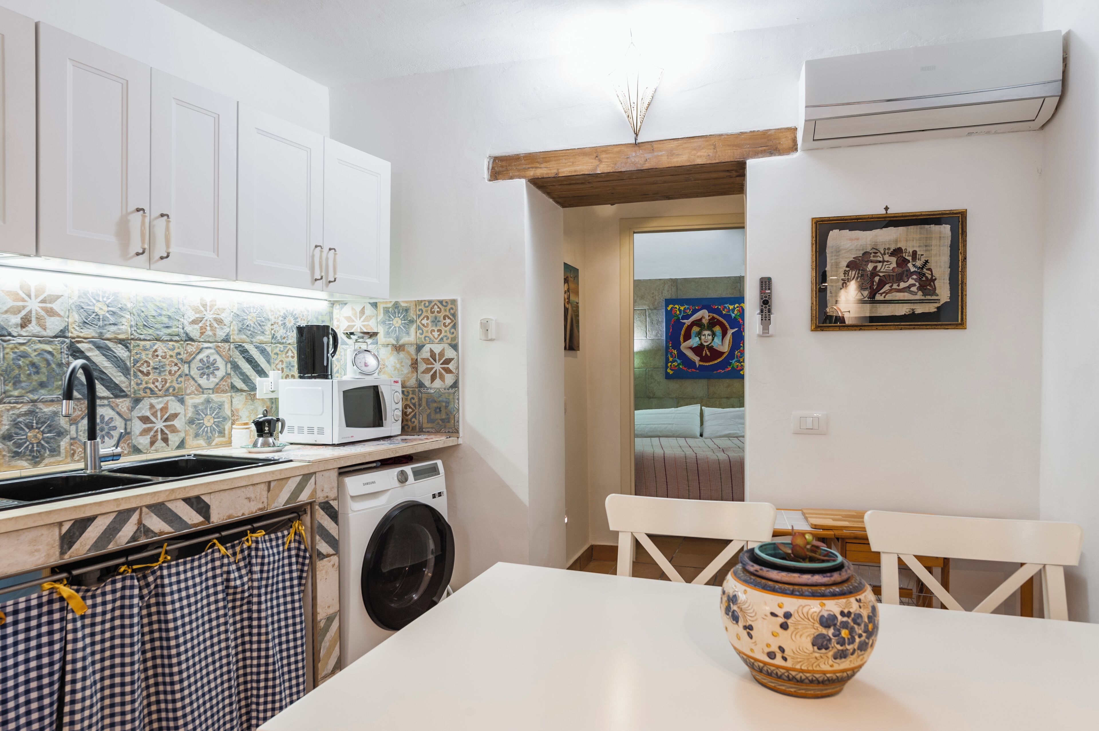 Une cuisine avec des meubles blancs, un four à micro-ondes, un lave-linge et un dosseret carrelé.