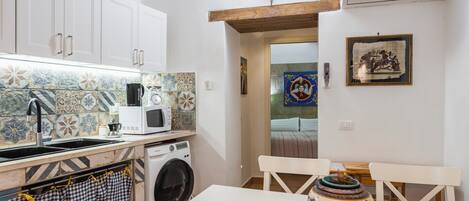 Une cuisine avec des meubles blancs, un four à micro-ondes, un lave-linge et un dosseret carrelé.
