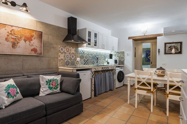A compact kitchen with a dining area, a washing machine, and a sofa with decorative pillows. - La casa di Rosa 1833 by Wonderful Italy (Syracuse)