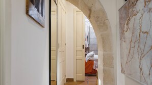 A hallway with a tiled floor, white walls, and an archway leading to a bedroom with a bed and a window. - La casa di Rosa 1833 by Wonderful Italy (Syracuse)