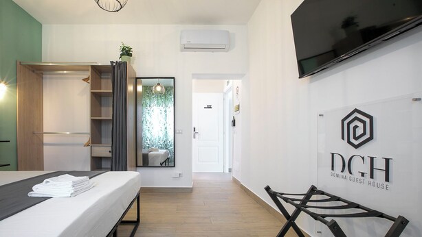 Una habitación de hotel moderna con una cama, un armario, un espejo, un televisor y un cartel para DCH Domina Guest House.