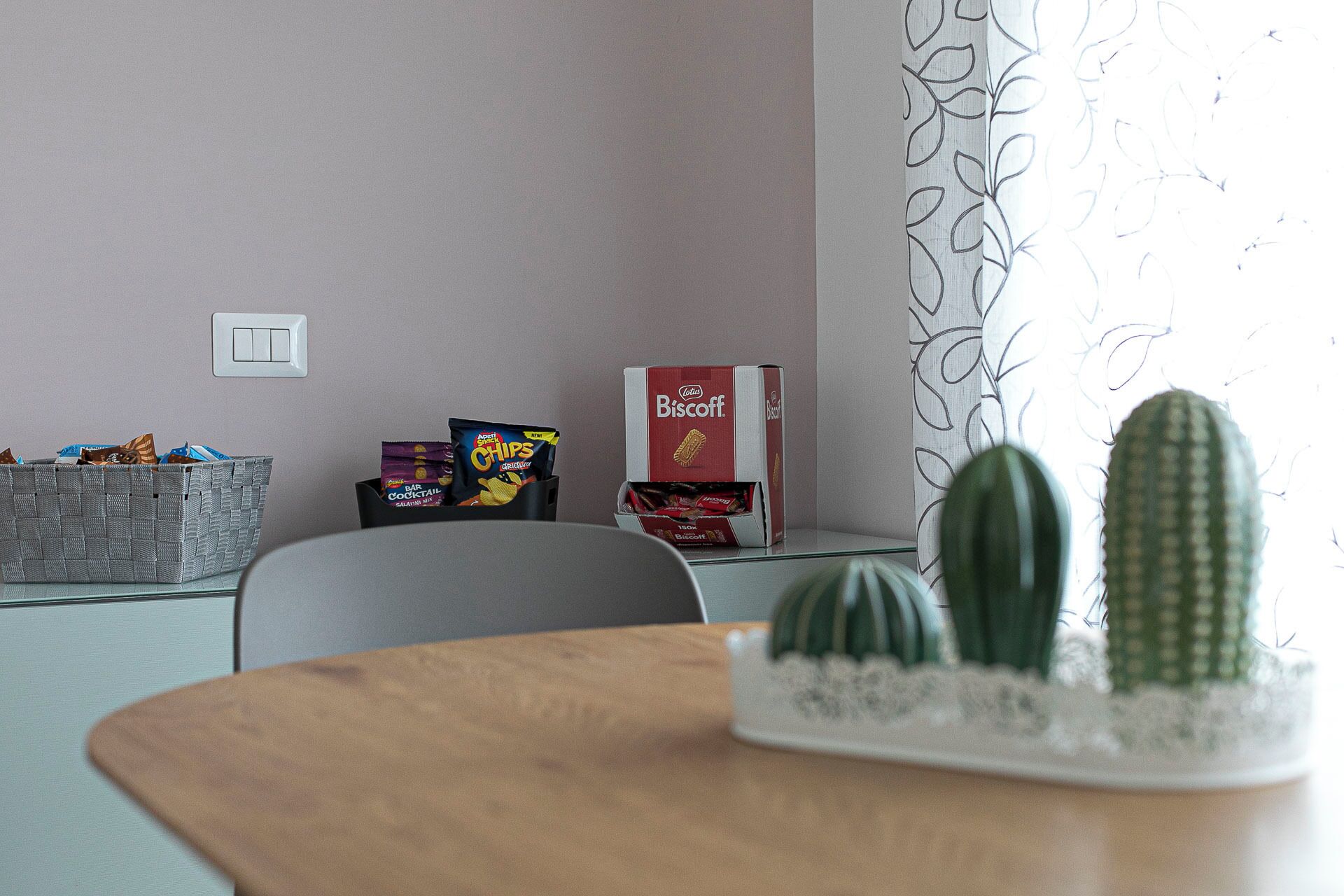 A room with a table, two cacti, a basket with snacks, and a box of Biscuits.