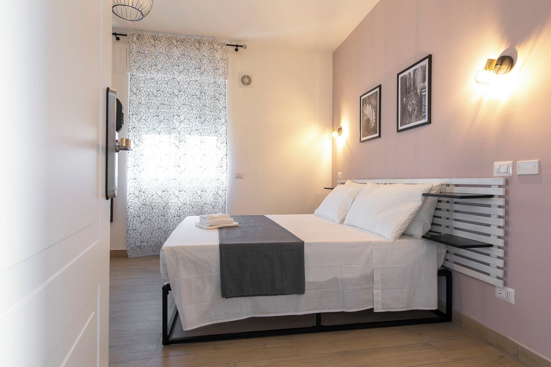 A bedroom with a bed, a bedside table, a wall-mounted heater, and two framed pictures.