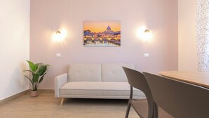 A room with a sofa, a dining table, and a potted plant.