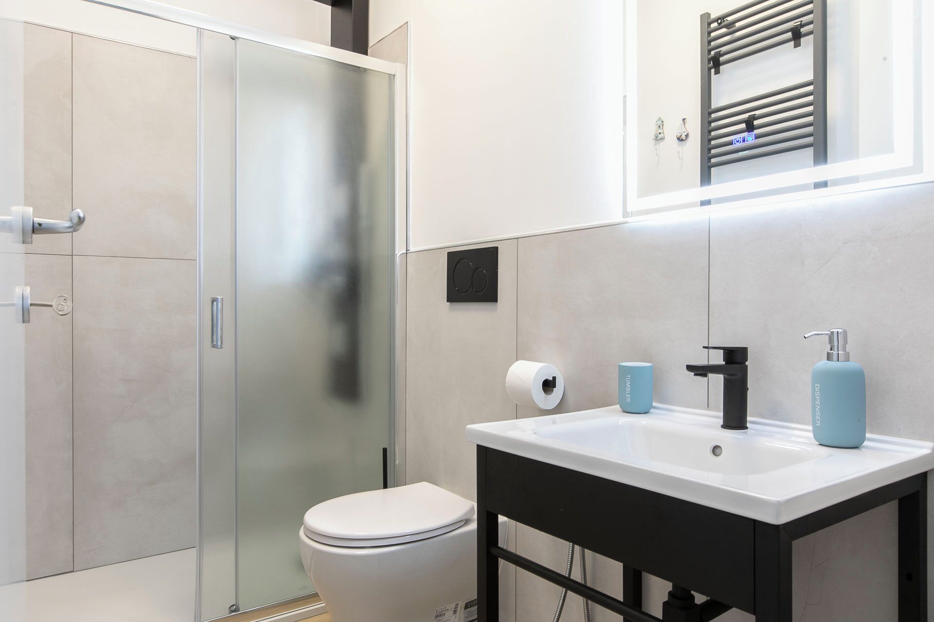 Ein modernes Badezimmer mit Duschkabine aus Glas, einer weißen Toilette, einem schwarzen Waschbecken mit Spiegel und einem Handtuchhalter über dem Waschbecken.