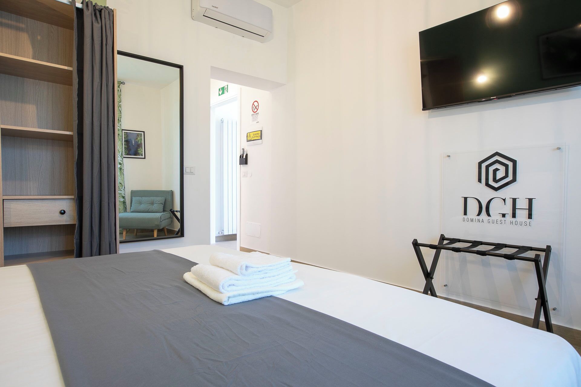 A hotel room with a bed, a TV, a mirror, and a sign for the Domina Guest House.