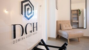 Un interior moderno con el logotipo de 'DOMINA GUEST HOUSE' y una zona de estar minimalista con un sofá y un espejo.