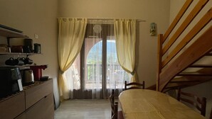 Una stanza accogliente e intima con un letto, una sedia di legno, una scrivania con una macchina per caffè e una finestra con tende.