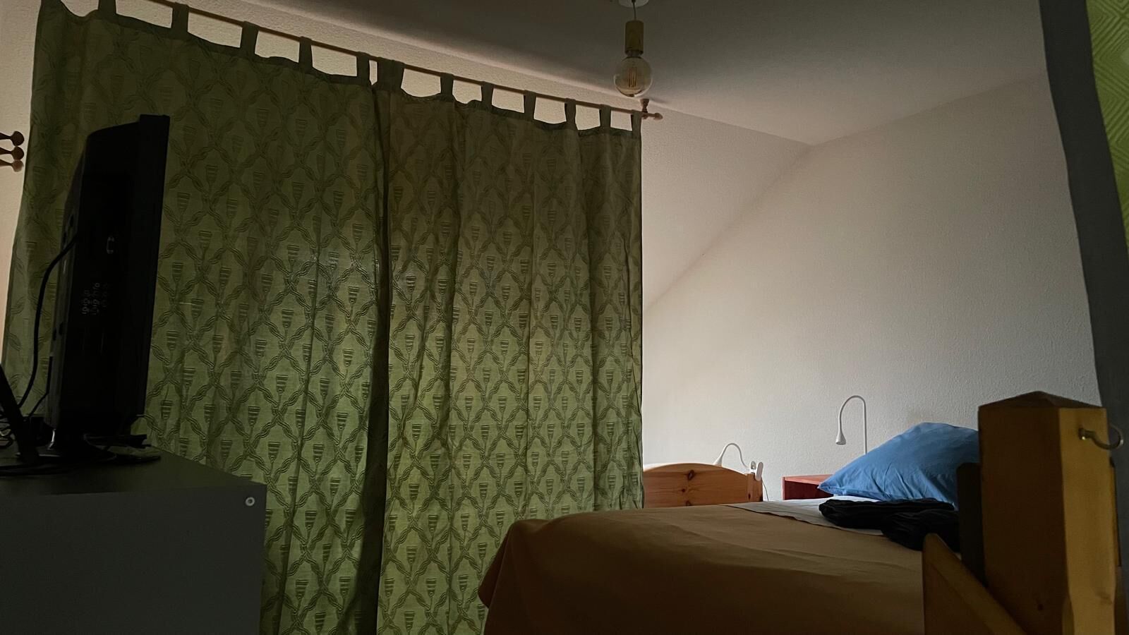 A bedroom with a bed, a desk, a chair, a television, and a curtain.