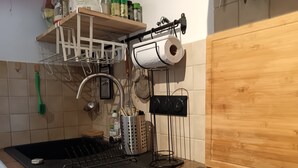 Una cucina con un piano di lavoro nero, un espositore per piatti, una rastrelliera per pentole pensili e un armadietto in legno.