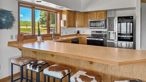 Een moderne keuken met houten kastjes, een groot eiland met barkrukken, roestvrijstalen apparatuur en uitzicht op de buitenruimte.