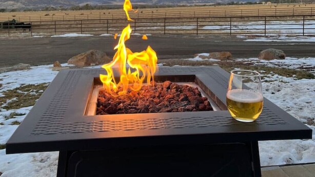 Een vierkante vuurkuip met vlammen, een glas bier en een uitzicht op besneeuwde bergen op de achtergrond.