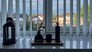 A window with white blinds, a black lantern, a vase with dried flowers, and a tall black vase on a windowsill. - Luxury Holiday Apartments (Manchester)