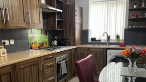 A modern kitchen with wooden cabinets, a tiled backsplash, and a dining area with a glass table and red chairs. - Luxury Holiday Apartments (Manchester)