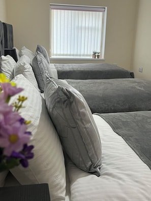 A hotel room with two beds, a window with blinds, and a small plant on the windowsill. - Luxury Holiday Apartments (Manchester)