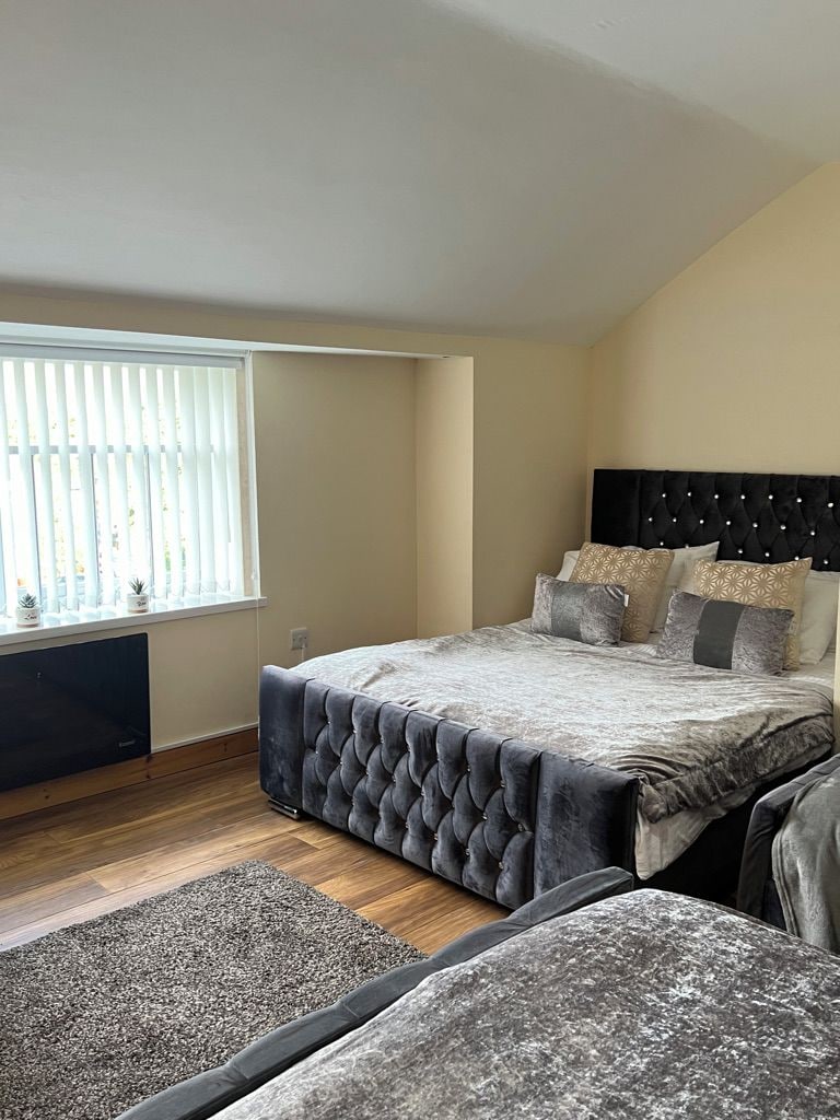 A bedroom with a bed, a window with blinds, a radiator, and a small plant on the windowsill.