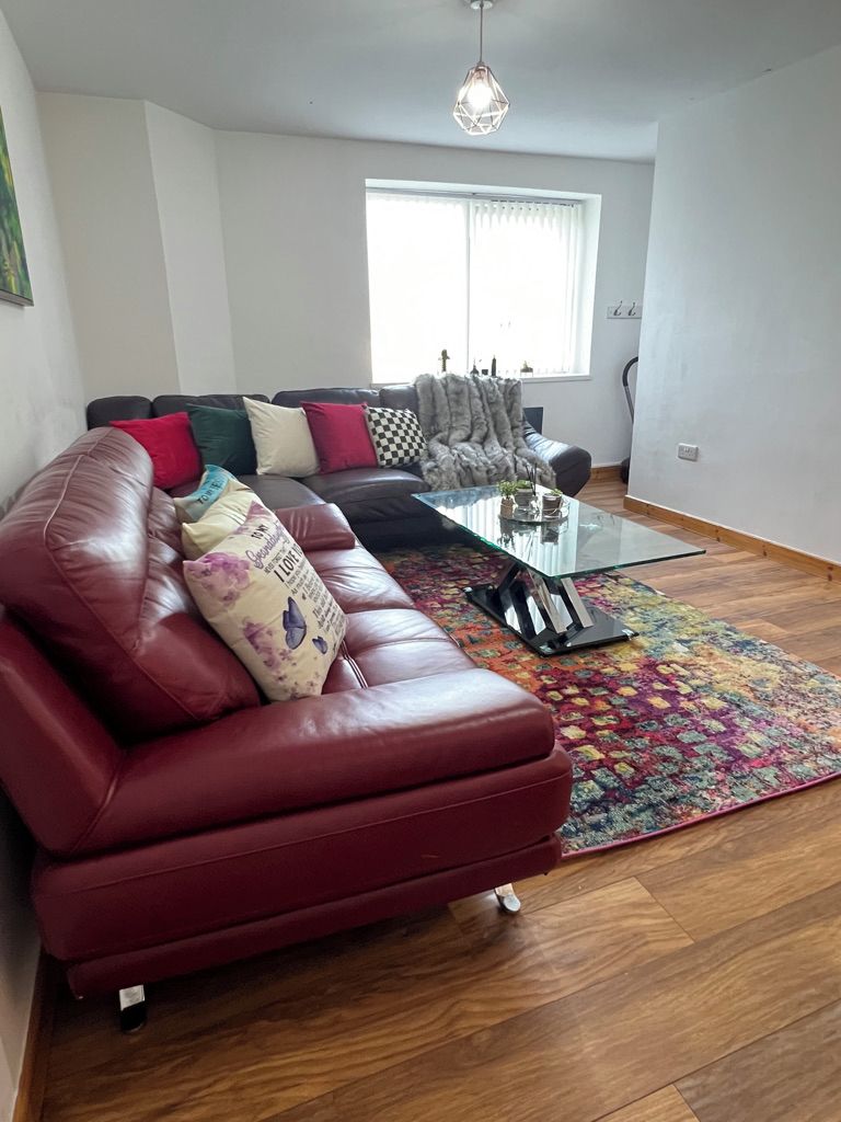 A living room with a red leather sofa, a glass coffee table, and a colorful rug.
