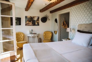 Un dormitorio con una cama grande, dos sillones, una mesita y un perchero en la pared.