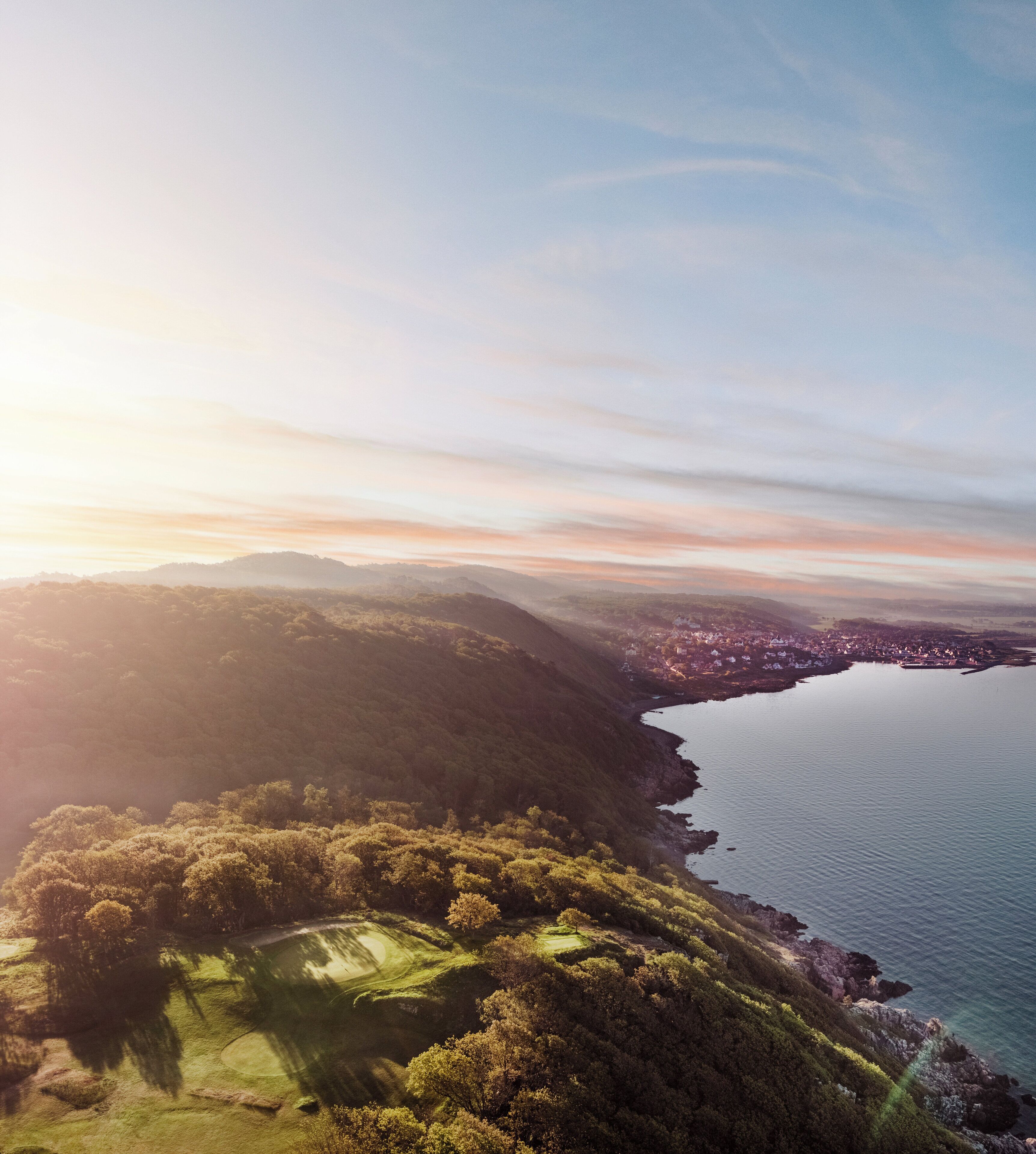 Vista aérea de una zona costera con un campo de golf, un pueblo y una extensa masa de agua.