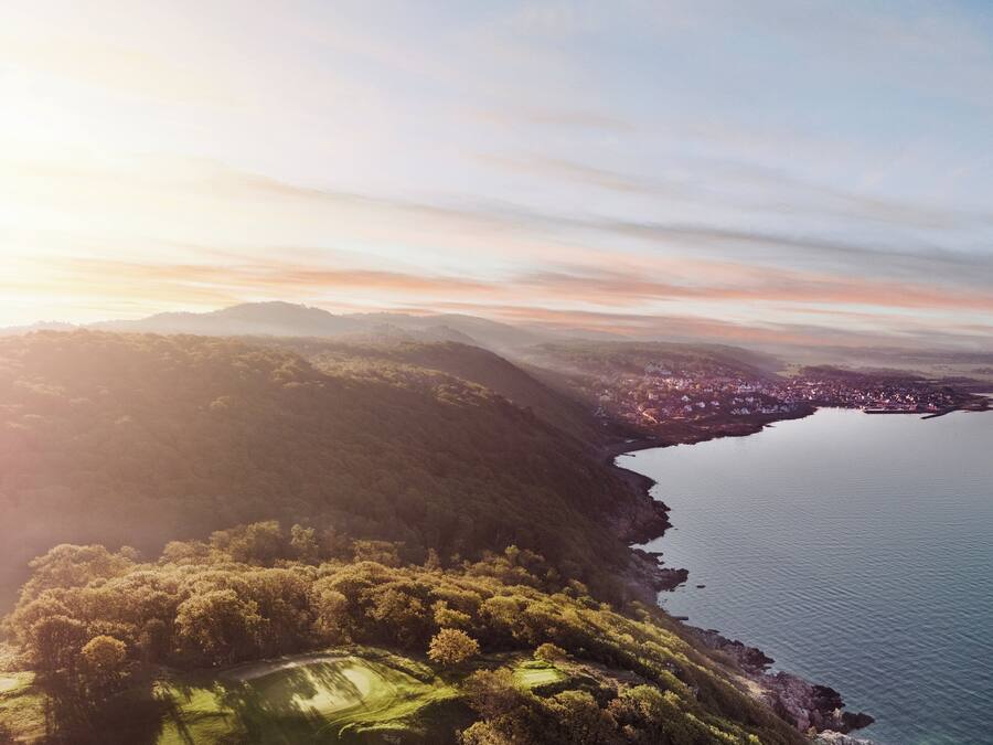 Vista aérea de una zona costera con un campo de golf, un pueblo y una extensa masa de agua.