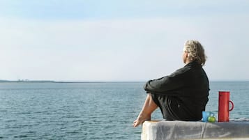 Una persona sentada sobre un borde de hormigón junto al mar, mirando al agua.