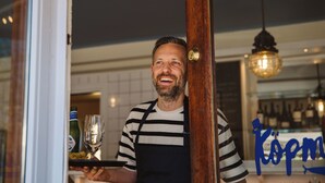 A person holding a tray with a bottle and a glass, standing in a doorway with a wooden frame. - Köpmans - Boutique Hotel (Hoganas)