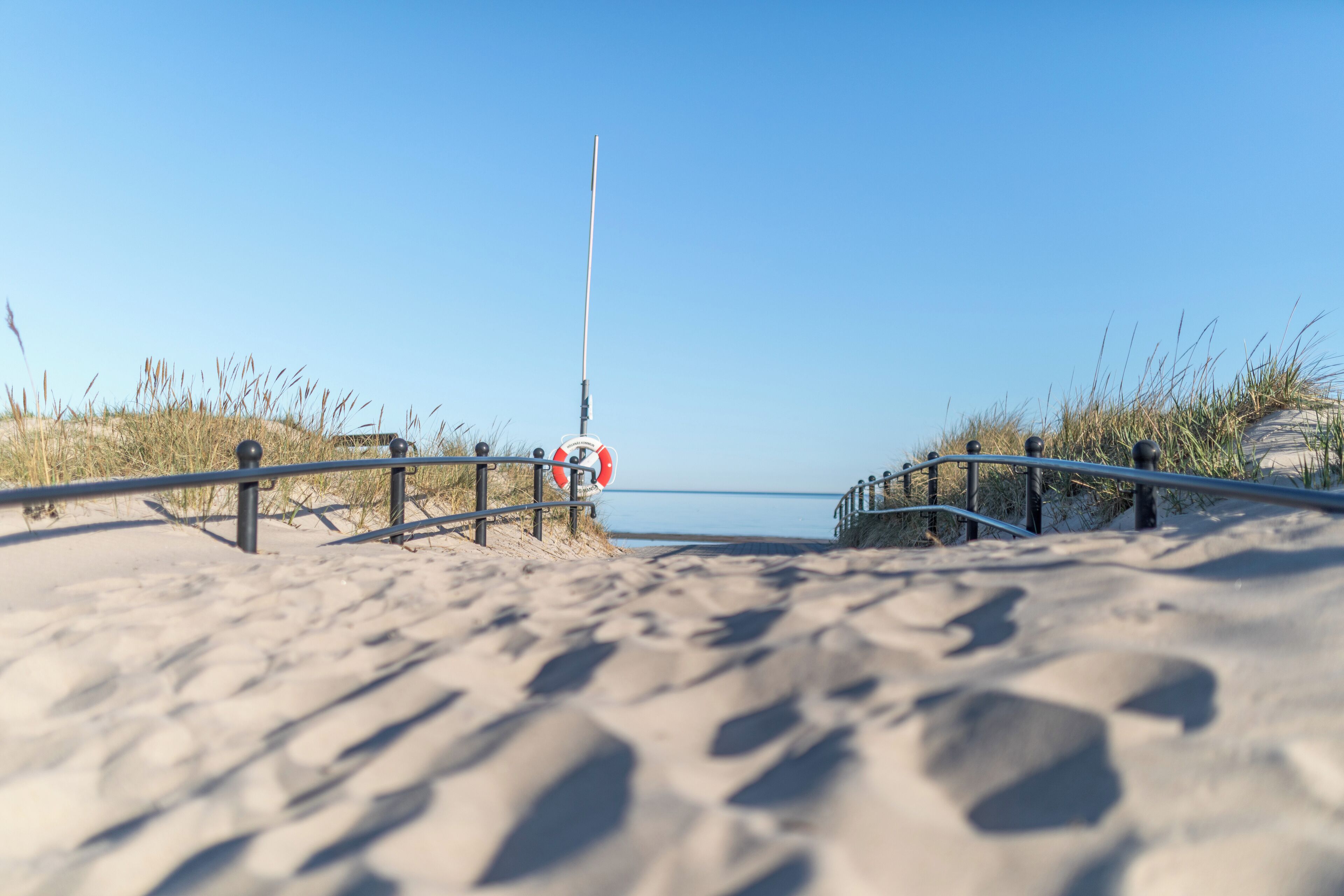 Ein Sandstrand mit Metallgeländer und einem Rettungsschwimmer-Schild.