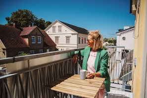 A balcony with a wooden table and a striped mug, overlooking a street with traditional buildings. - Köpmans - Boutique Hotel (Hoganas)